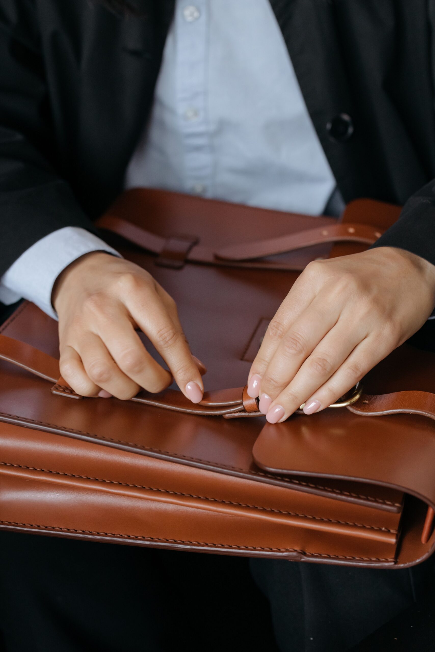Woman fastening the strap closure on a brown leather briefcase during a business meeting.